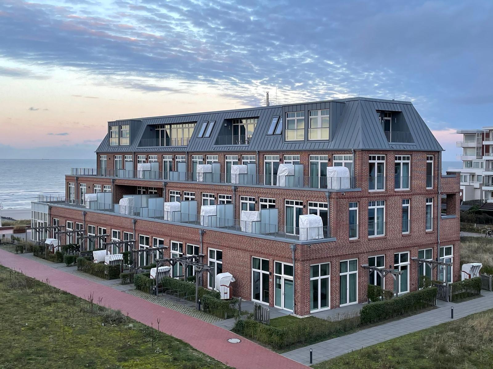 Das Aparthotel Anna Dune mit Glasfassade und Balkonen unter blauem Himmel.