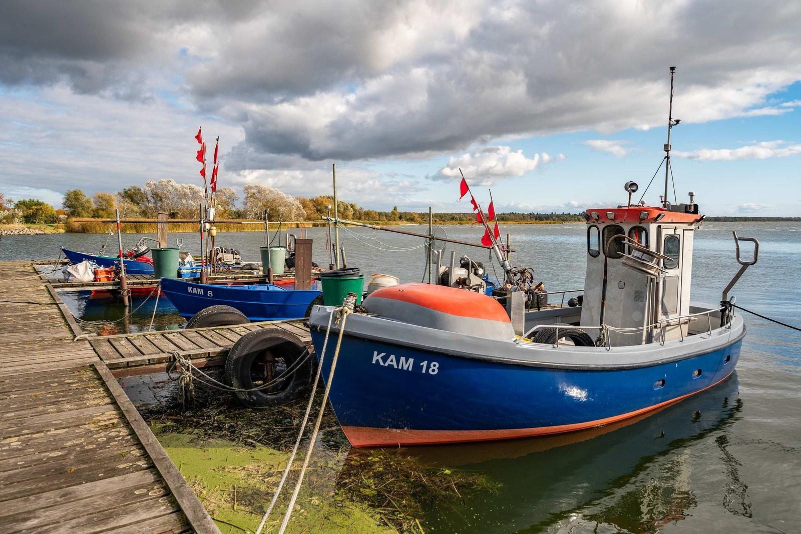 Hafen mit blauen Booten und roten Flaggen am Wasser.