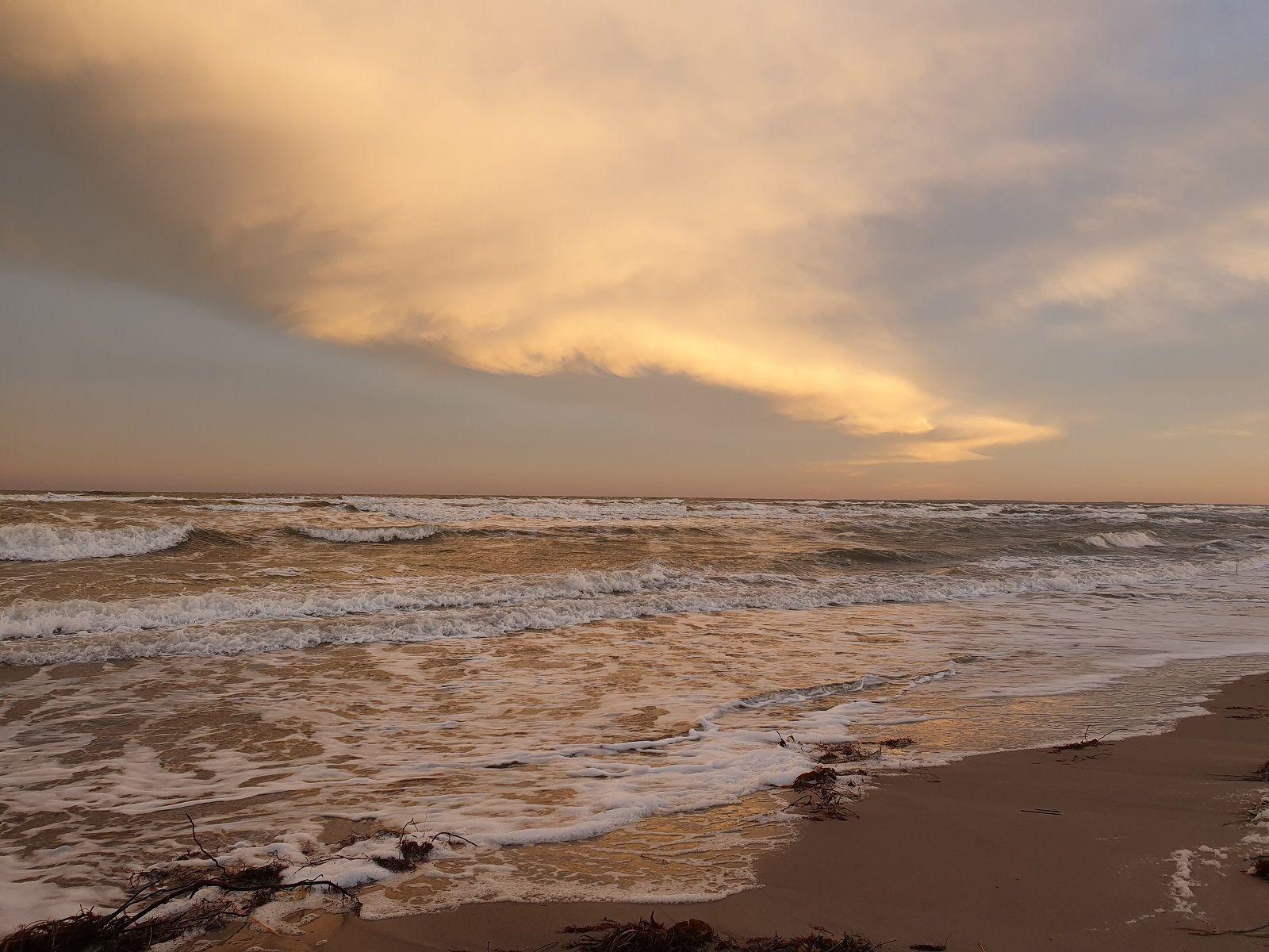 Strand mit weißen Häusern im Hintergrund und Steinen im Vordergrund.
