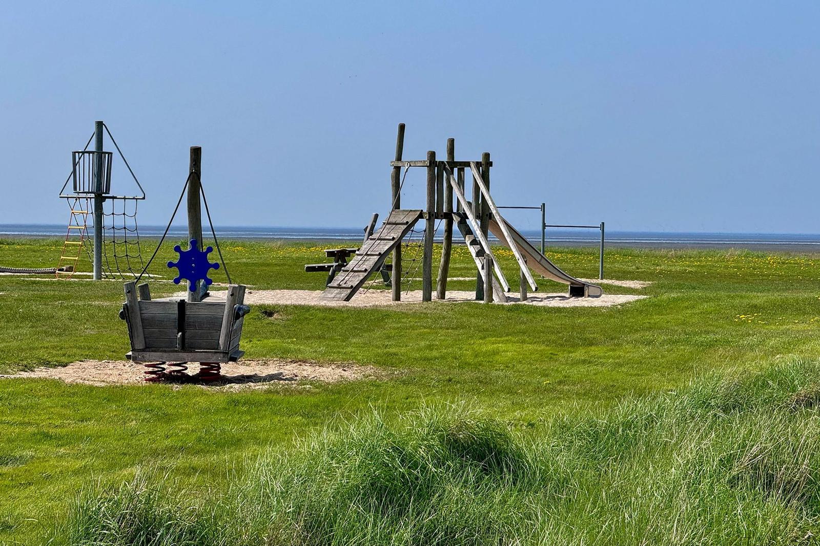Holzbrücke führt über Steine zum Meer unter blauem Himmel.