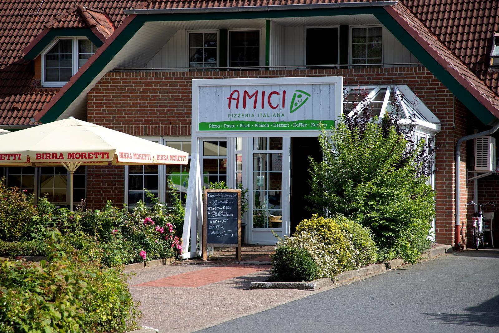 Red brick building with thatched roof and green accents, surrounded by greenery and a paved path.