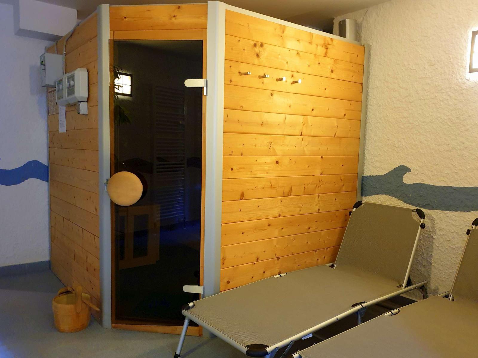 Zwei Liegestühle mit blau-weißem Stoff und eine Liege stehen in einem Raum mit Wandbildern und Pflanzen.