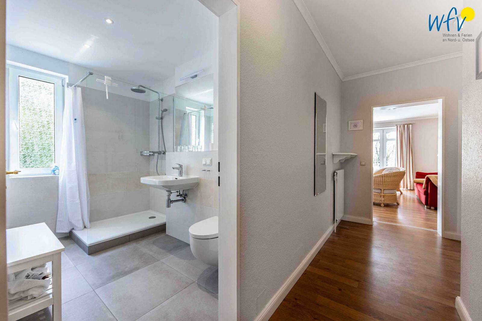 Eingangsbereich mit Spiegel, Heizkörper und Blick in Wohnzimmer mit Rattanmöbeln.