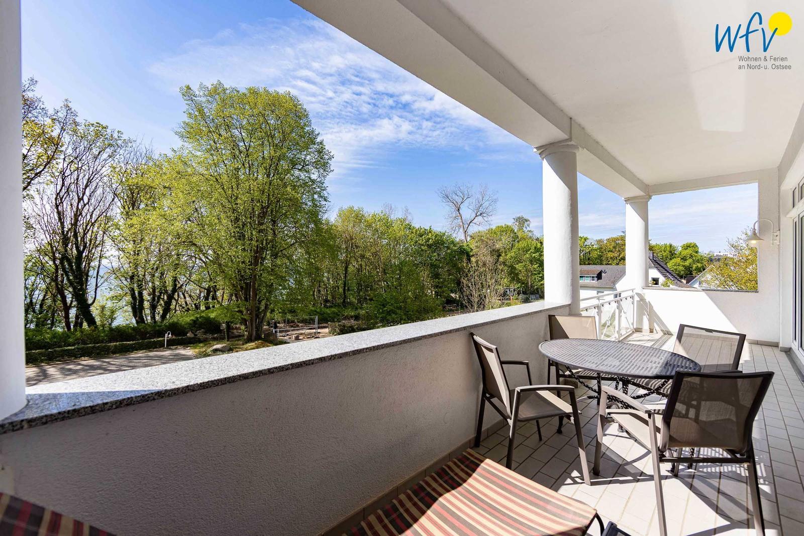 Terrasse mit Tisch und Stühlen, Blick auf Bäume und einen See.