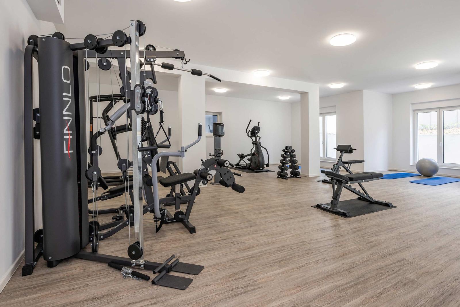 Fitnessraum mit Laufband, Ellipsentrainer und Gewichten.
