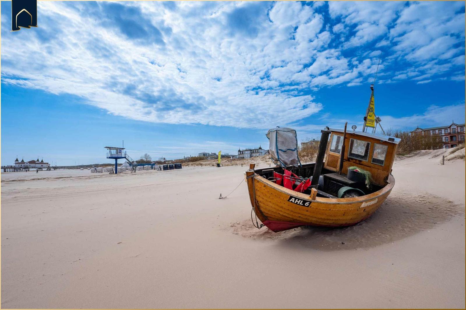Strand mit Strandkörben und Pier bei Sonnenuntergang. Hintergrund: weißes Gebäude mit Dächern.