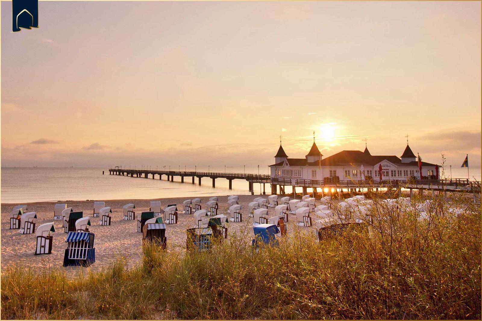 Sonnenuntergang über Strand und Pier mit Sanddünen im Vordergrund.