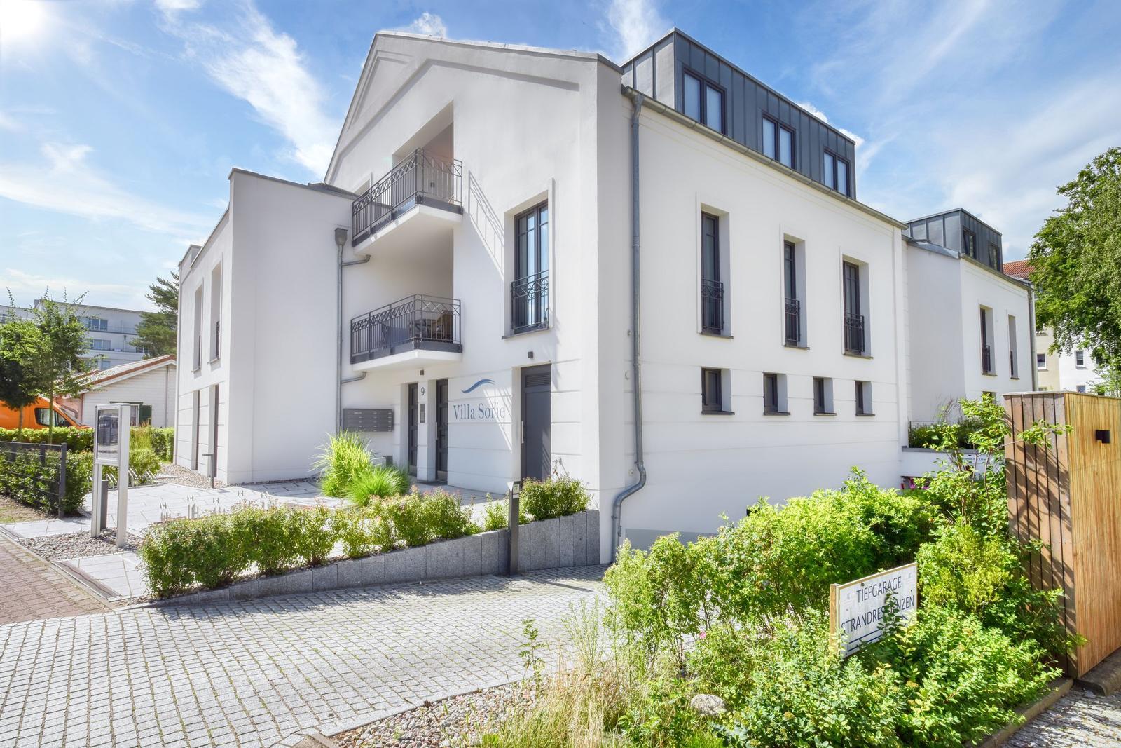 Moderne weiße Wohnanlage mit Balkonen und gepflegtem Gartenbereich.