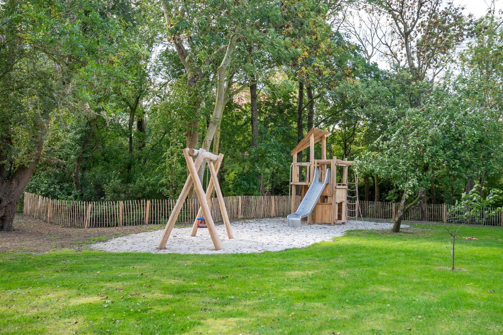 Spielplatz mit Sandkasten und Holzspielgeräten im Grünen.