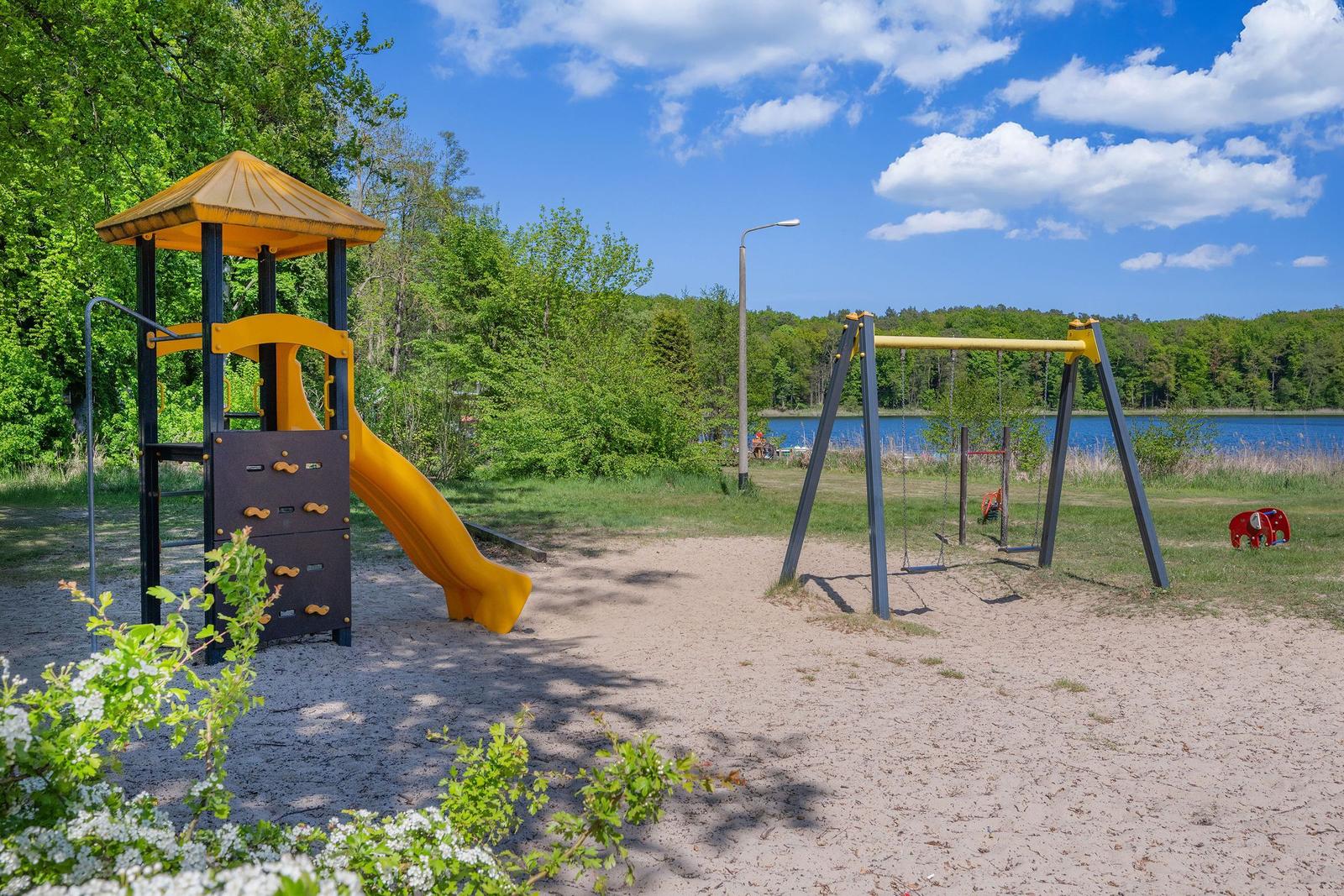 Zwei Bänke stehen am Strand eines Sees mit Wald im Hintergrund.