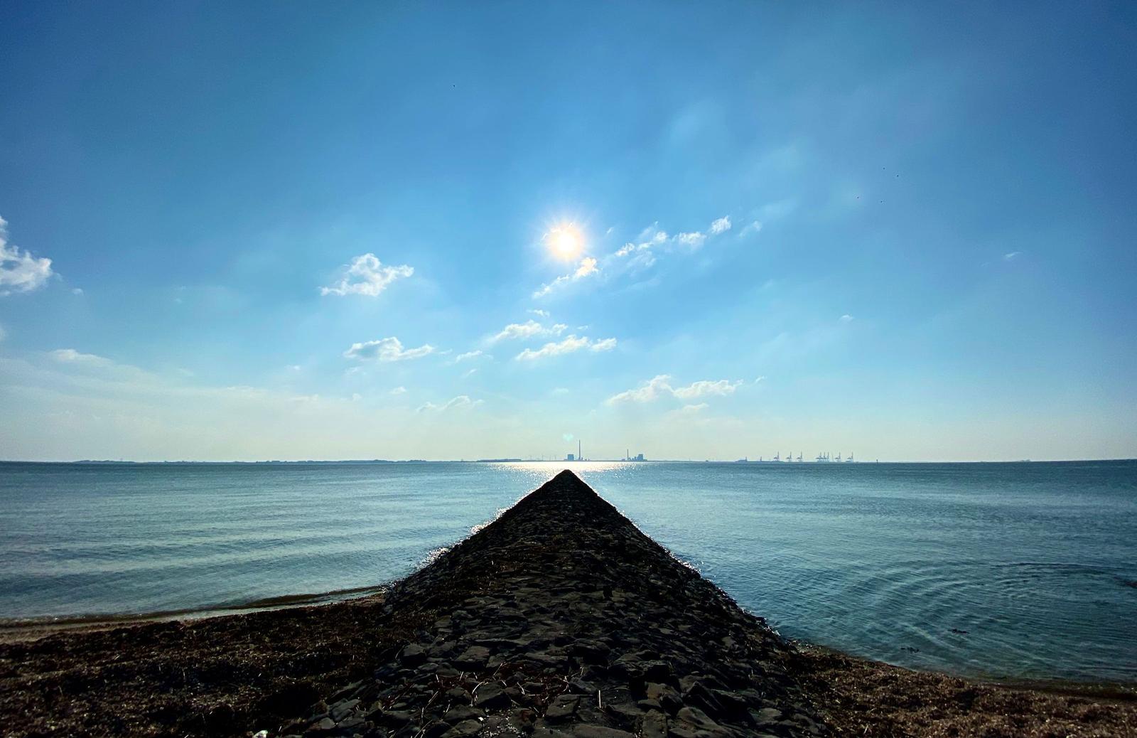 Strand mit Steinen und Wasser unter blauem Himmel mit Sonne und Wolken