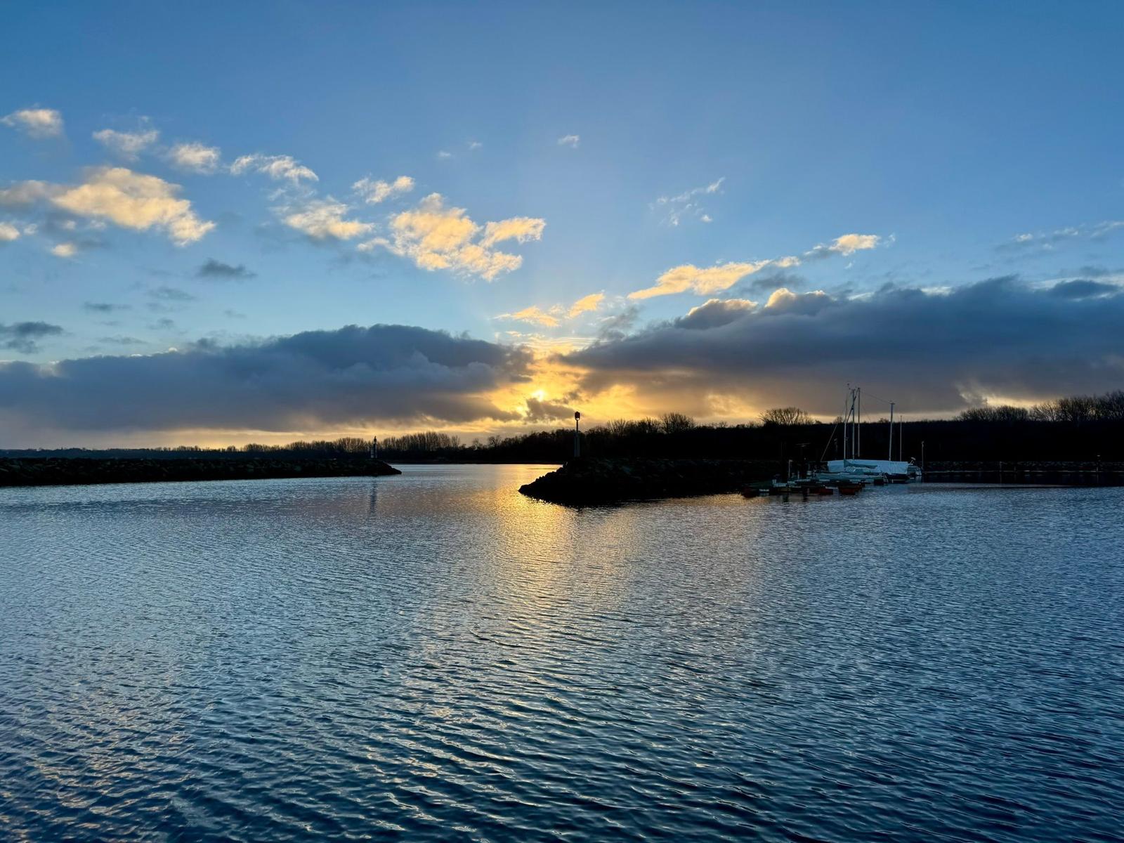 Sonnenuntergang über Marina mit Segelyachten und Spiegelungen im Wasser.
