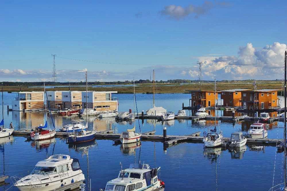 Fünf hölzerne Bootsboxen stehen auf dem Wasser. Jede hat eine Terrasse und Fenster.