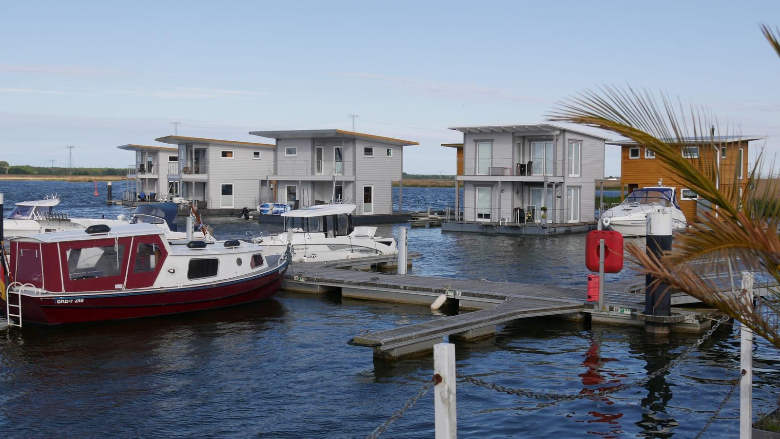 Häuser auf dem Wasser mit Bootsanlegern und Yachten im Hintergrund.