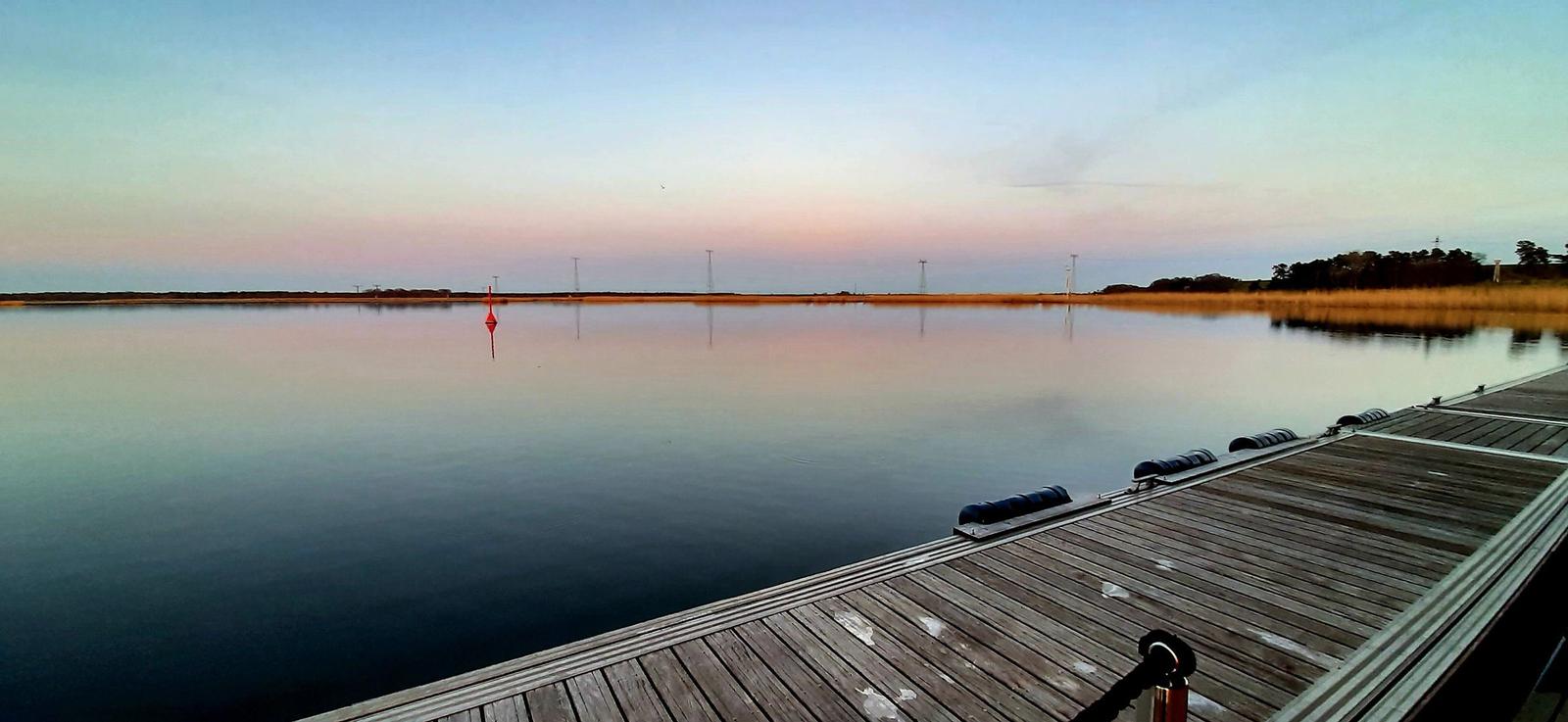 Sonnenuntergang über ruhigem Wasser mit Blick von einem Bootssteg.