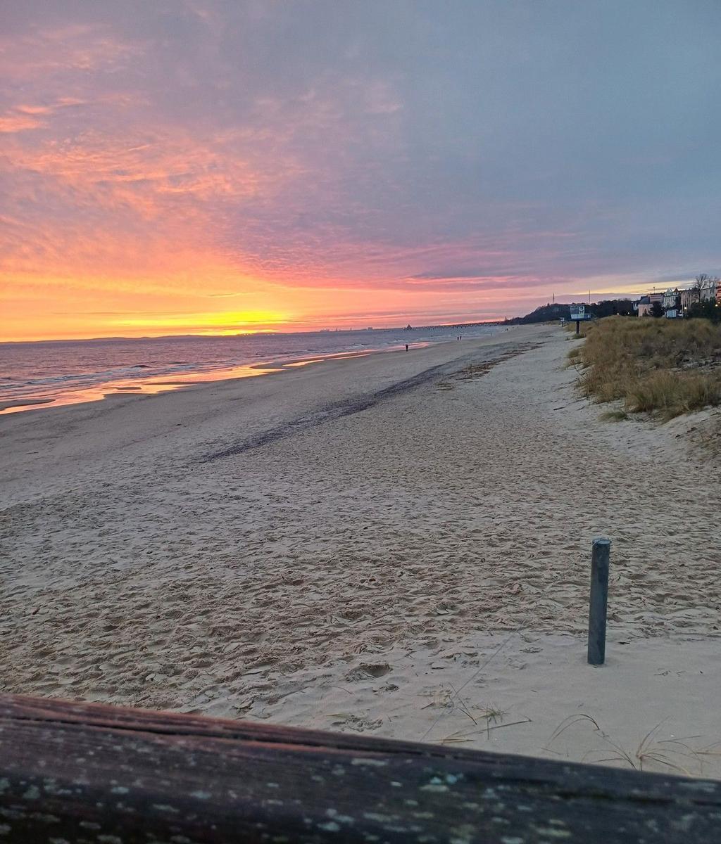 Sandweg führt zum Strand bei Sonnenuntergang mit farbenfrohem Himmel.