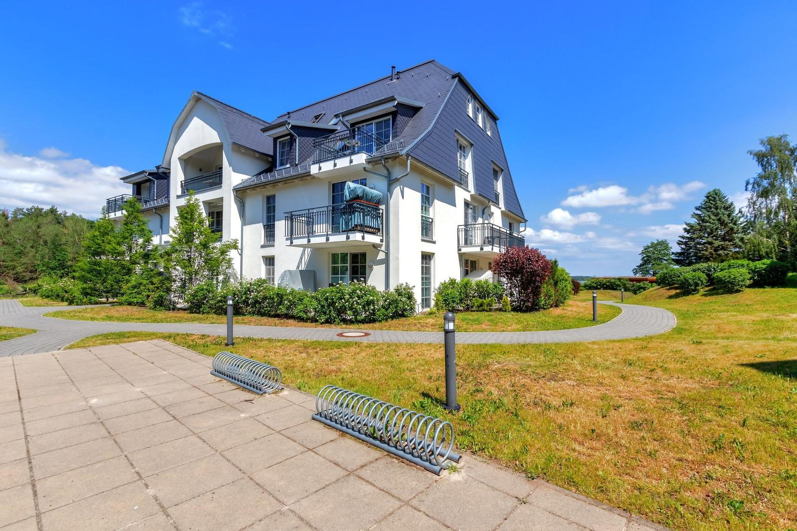 Wohnhaus mit Balkonen und Garten, Blick auf See unter blauem Himmel.