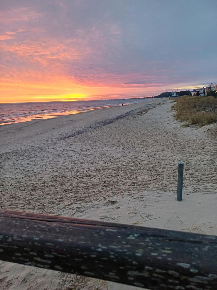 Strand mit Wellen und Sonnenuntergang im Hintergrund