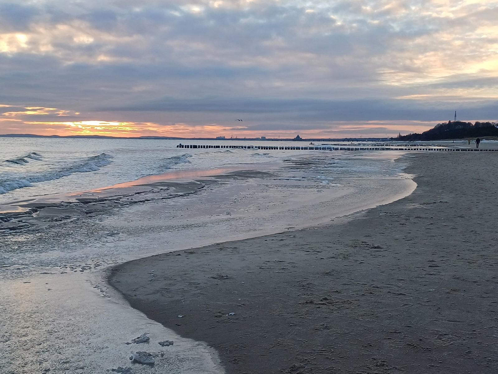 Strand mit Sand und ruhigem Wasser unter blauem Himmel.