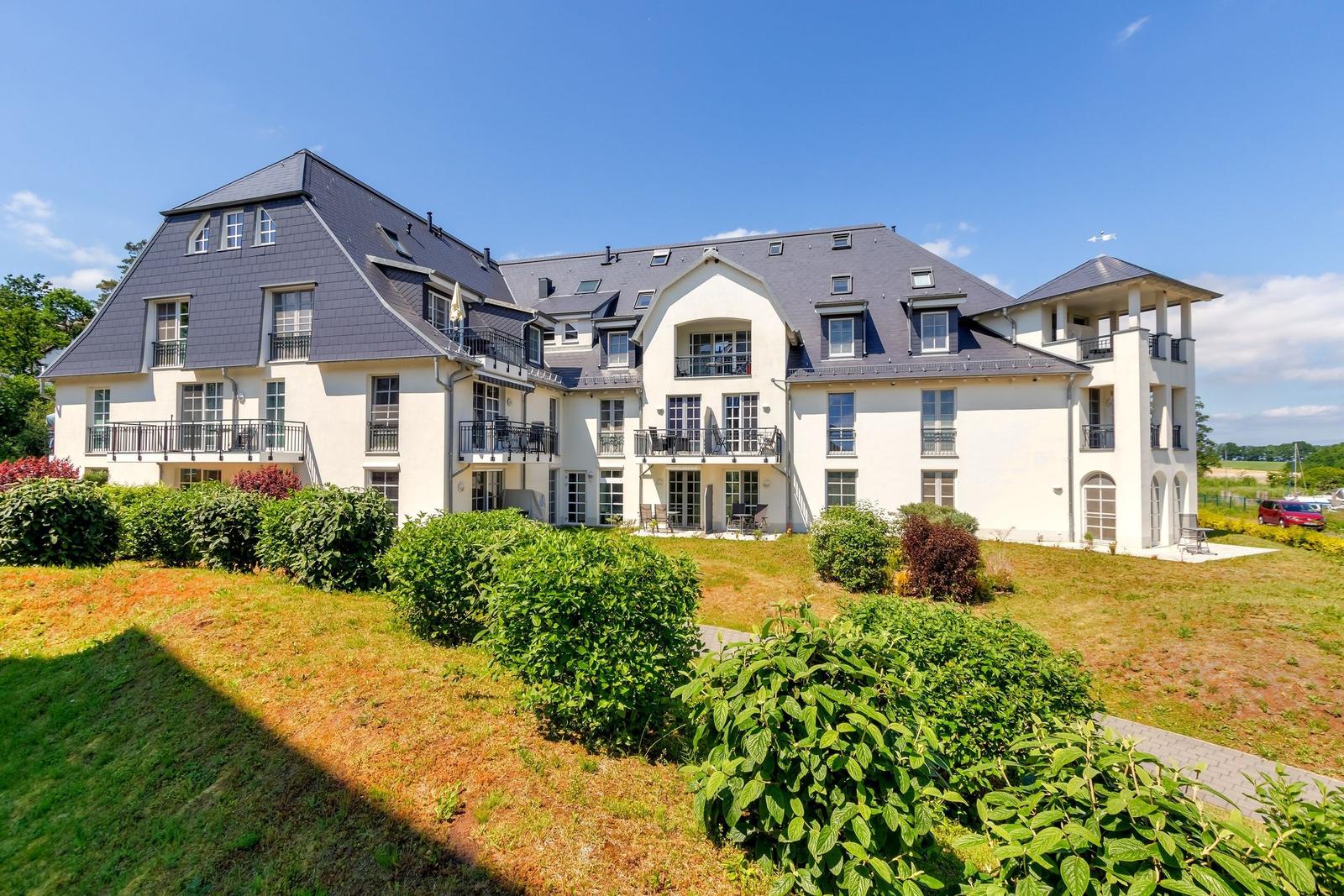Haus mit großem Garten und hohen Bäumen unter blauem Himmel.