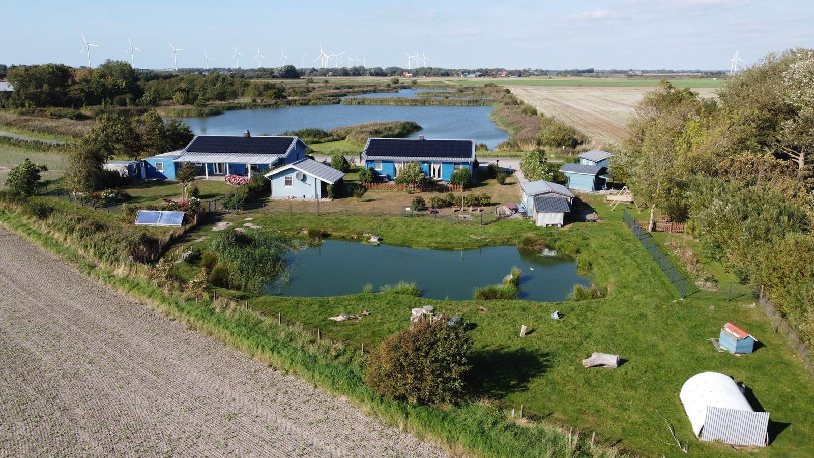 Aeriale Aufnahme von mehreren blauen Häusern mit Solaranlagen und einem Teich auf grünem Grund.