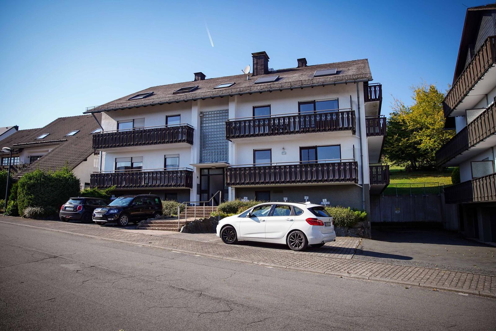 Wohnhaus mit Balkonen und gepflegtem Garten unter blauem Himmel.