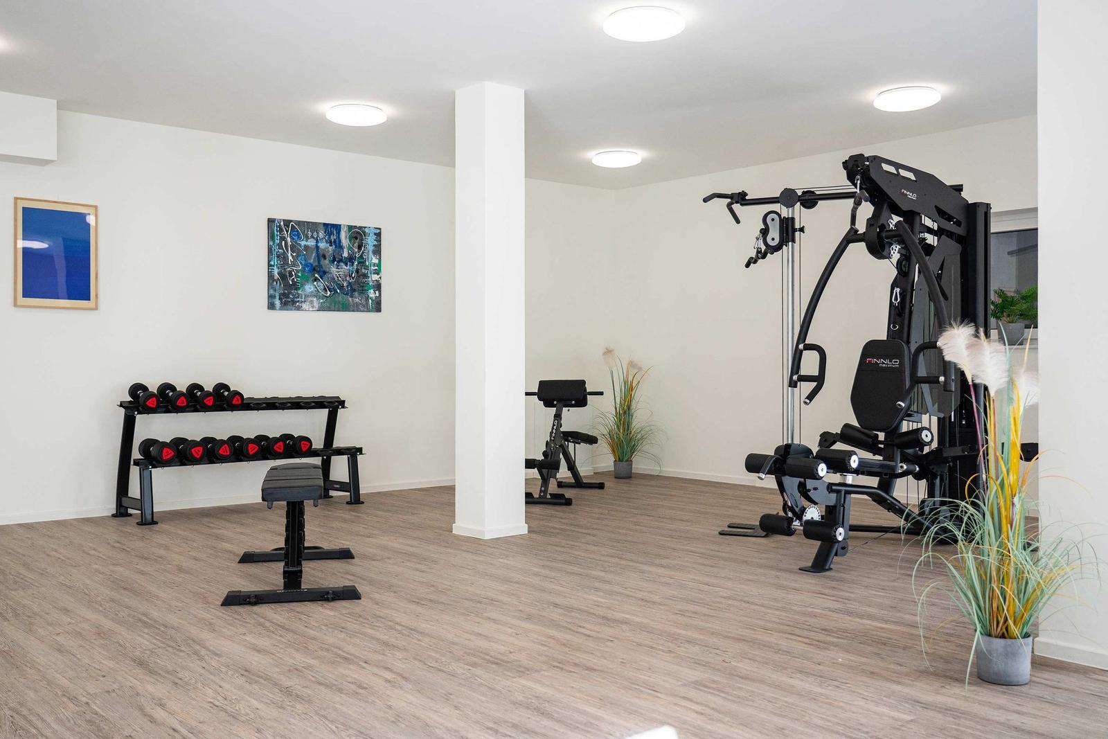 Fitnessraum mit zwei Geräten, Pflanzen und Fenster zur Außenseite.