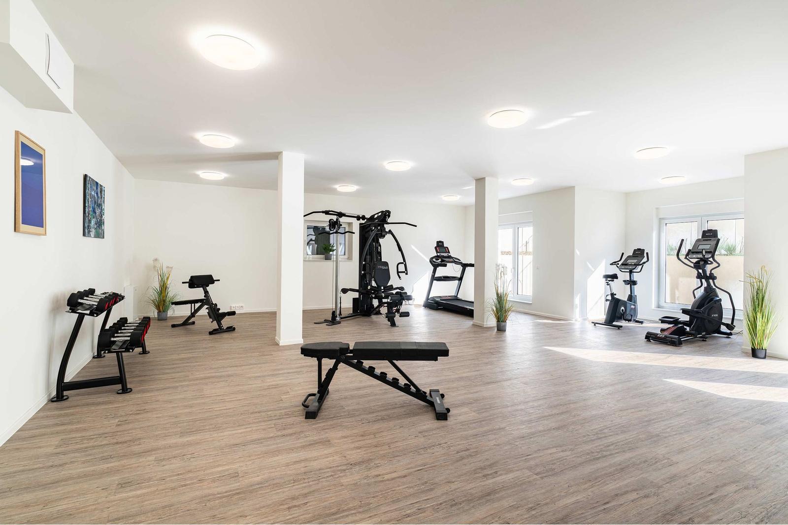 Fitnessraum mit Laufband, Kraftstation und Bank. Spiegel an den Wänden.