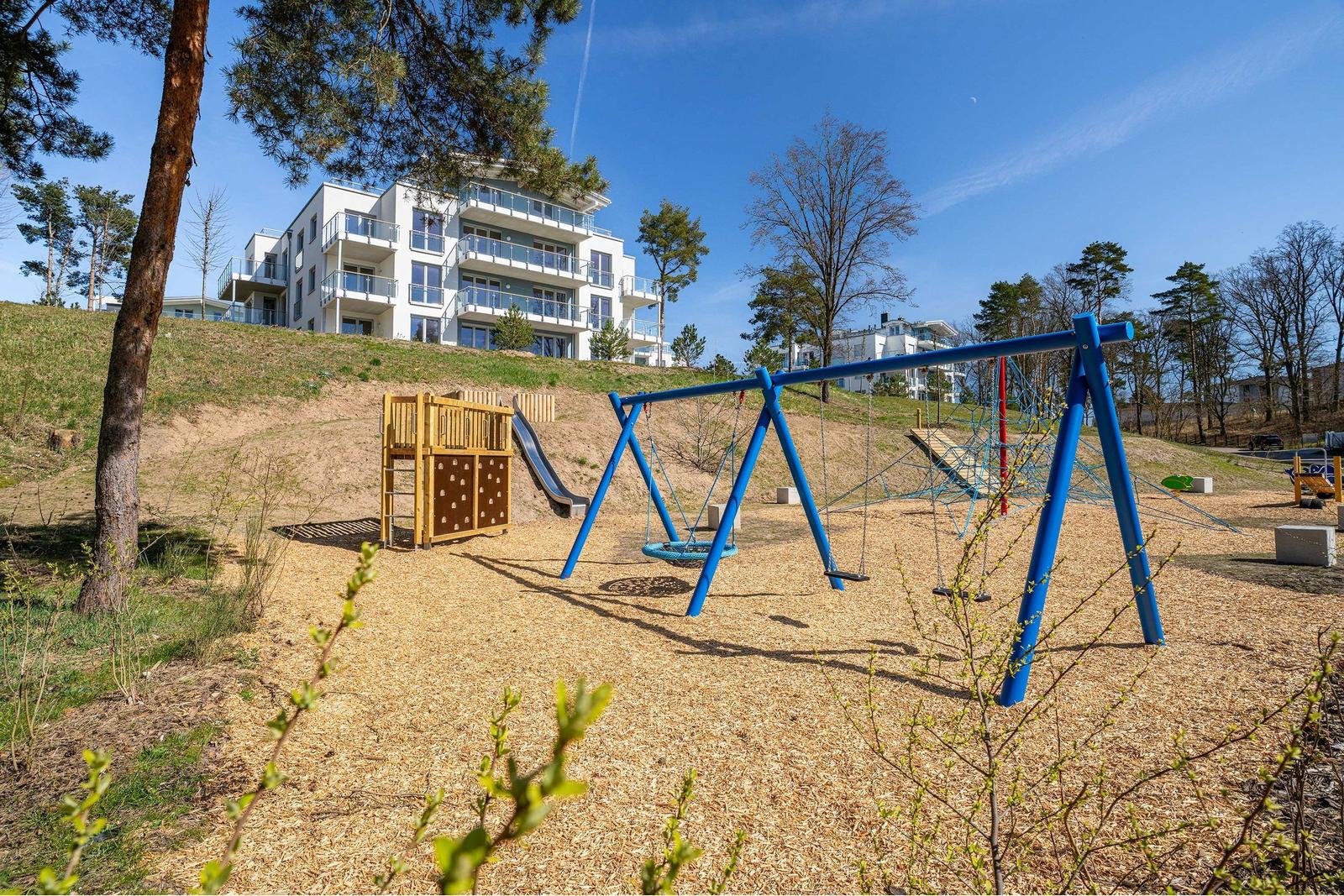 Kinderspielplatz mit Rutsche, Klettergerüst und Schaukel auf sandigem Boden.