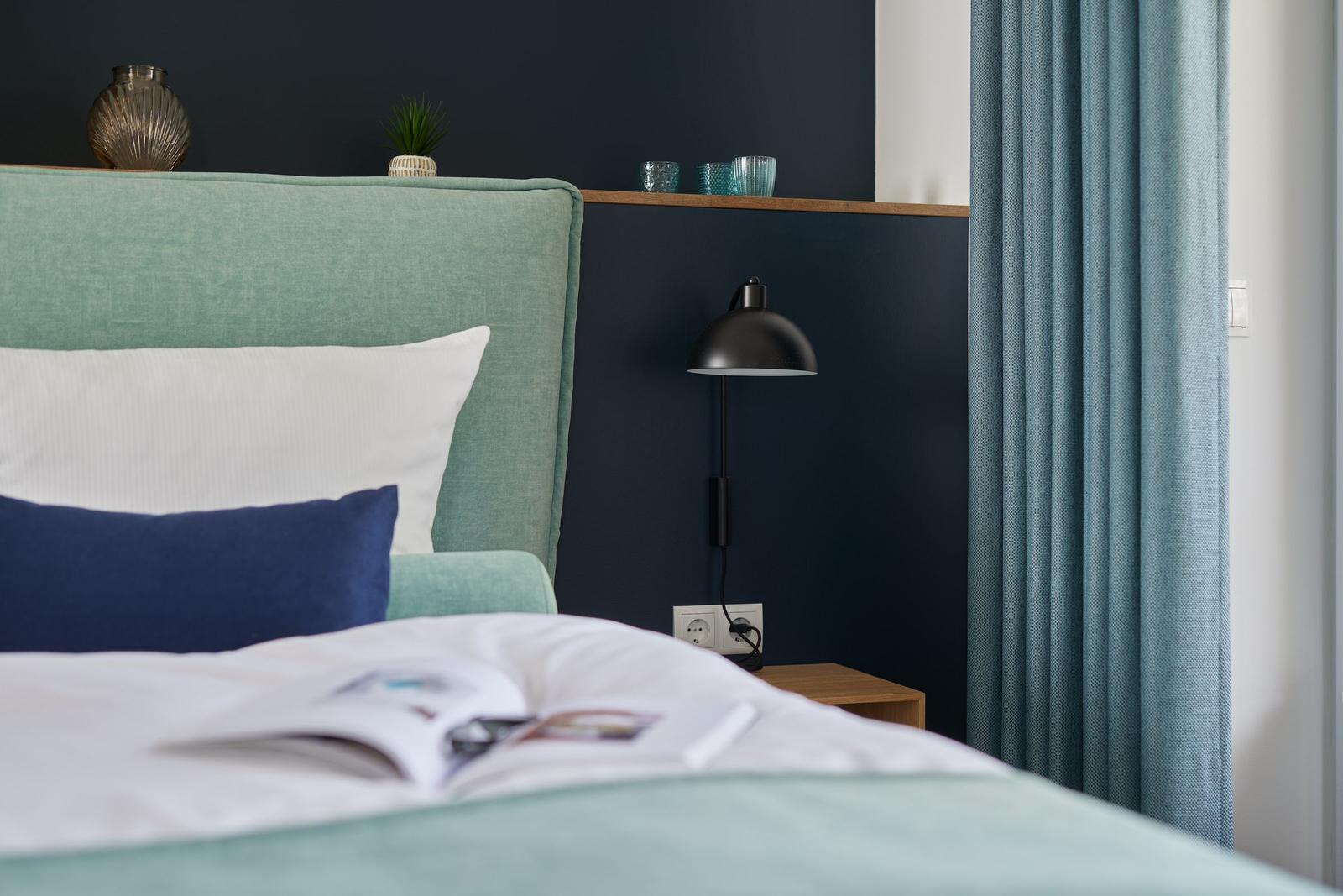 Schlafzimmer mit Bett, Wandspiegel und Tür zum Bad.