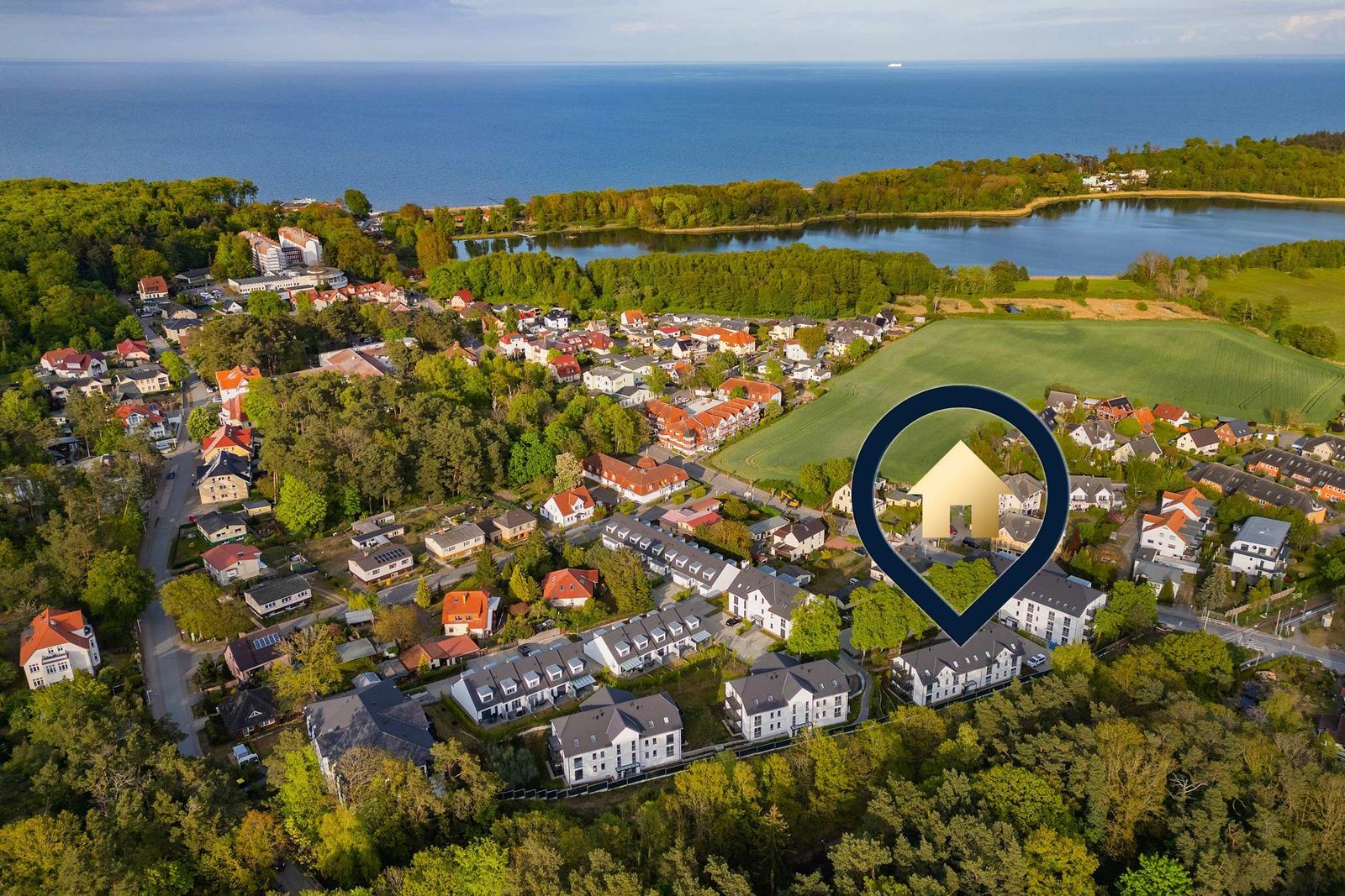 Luftbild von Wohnhäusern mit Wald und See im Hintergrund.