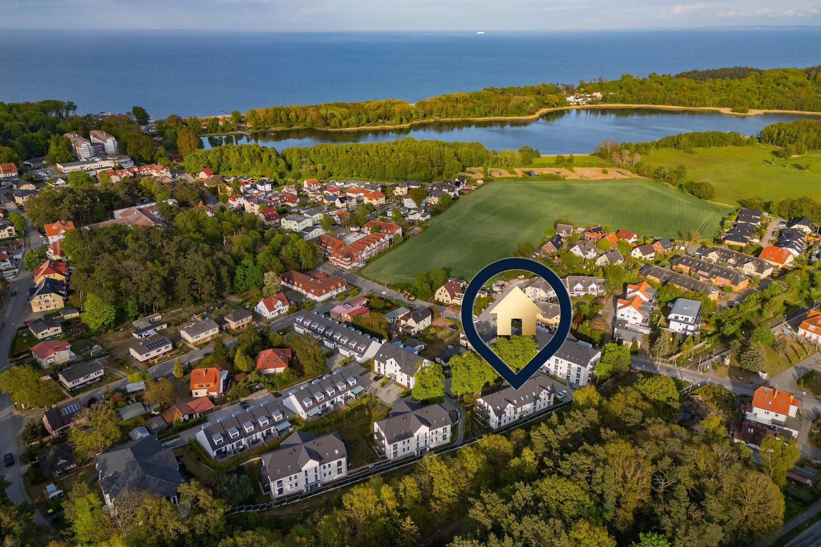 Luftbild eines Dorfes mit Häusern, Wäldern und einem See im Hintergrund.