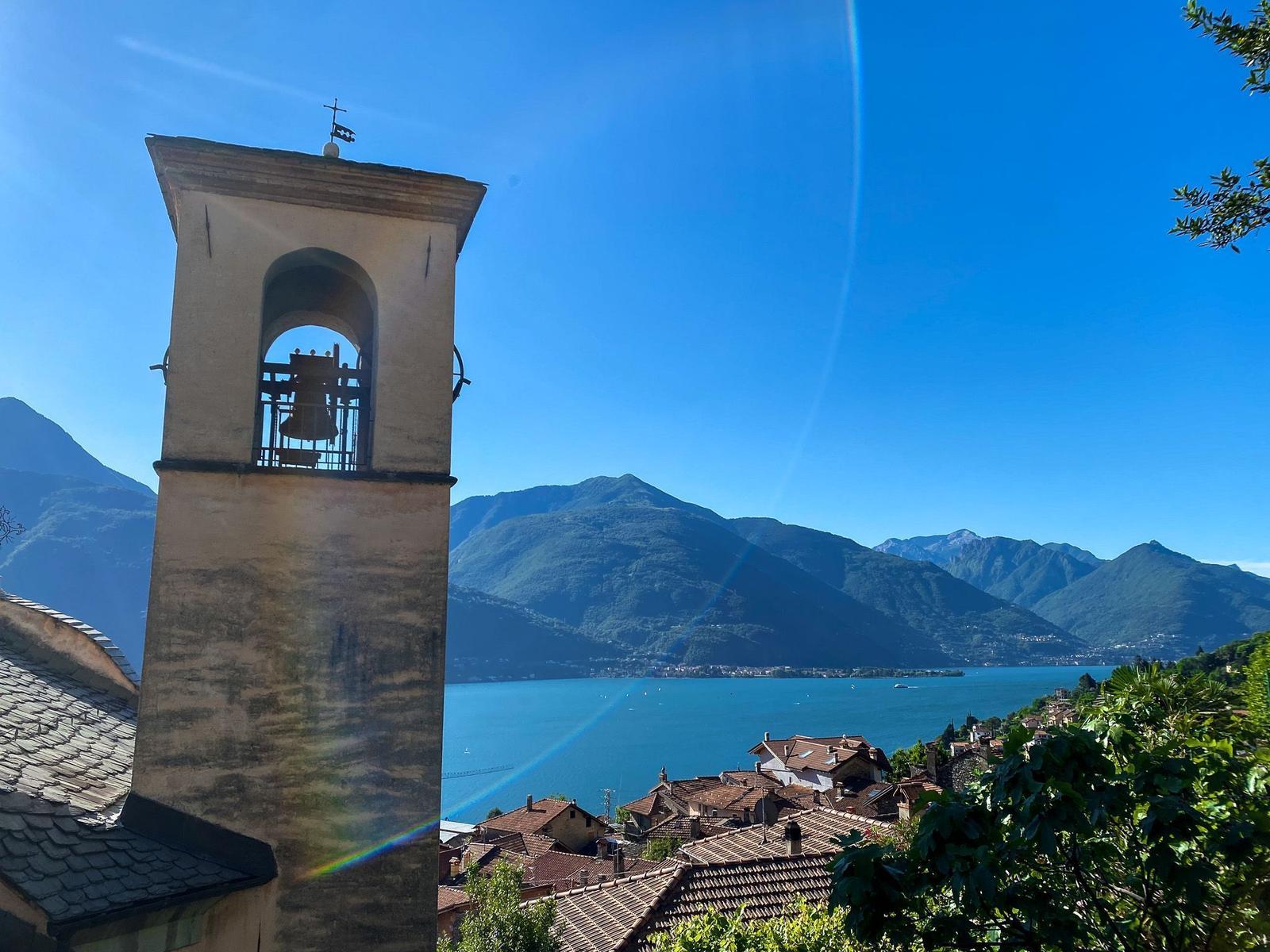 Weg entlang des Sees mit Blick auf Berge und Häuser.