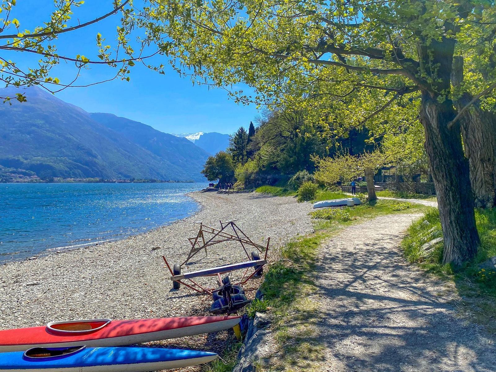 Strand mit Gästen, Booten und Bergen im Hintergrund.