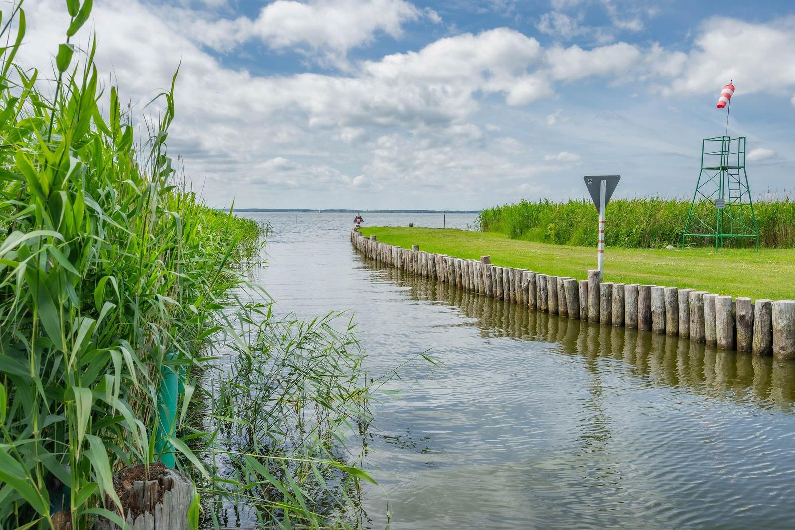 Ein weißes Motorboot liegt an einem Holzsteg im Wasser. Im Hintergrund sind Häuser und Gräser zu sehen.