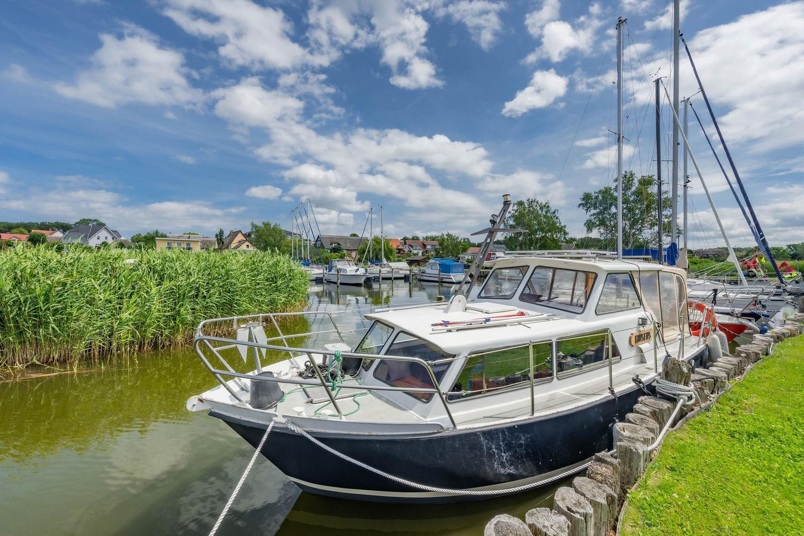 Holzsteg führt zwischen Yachten im Hafen. Blauer Himmel mit Wolken.