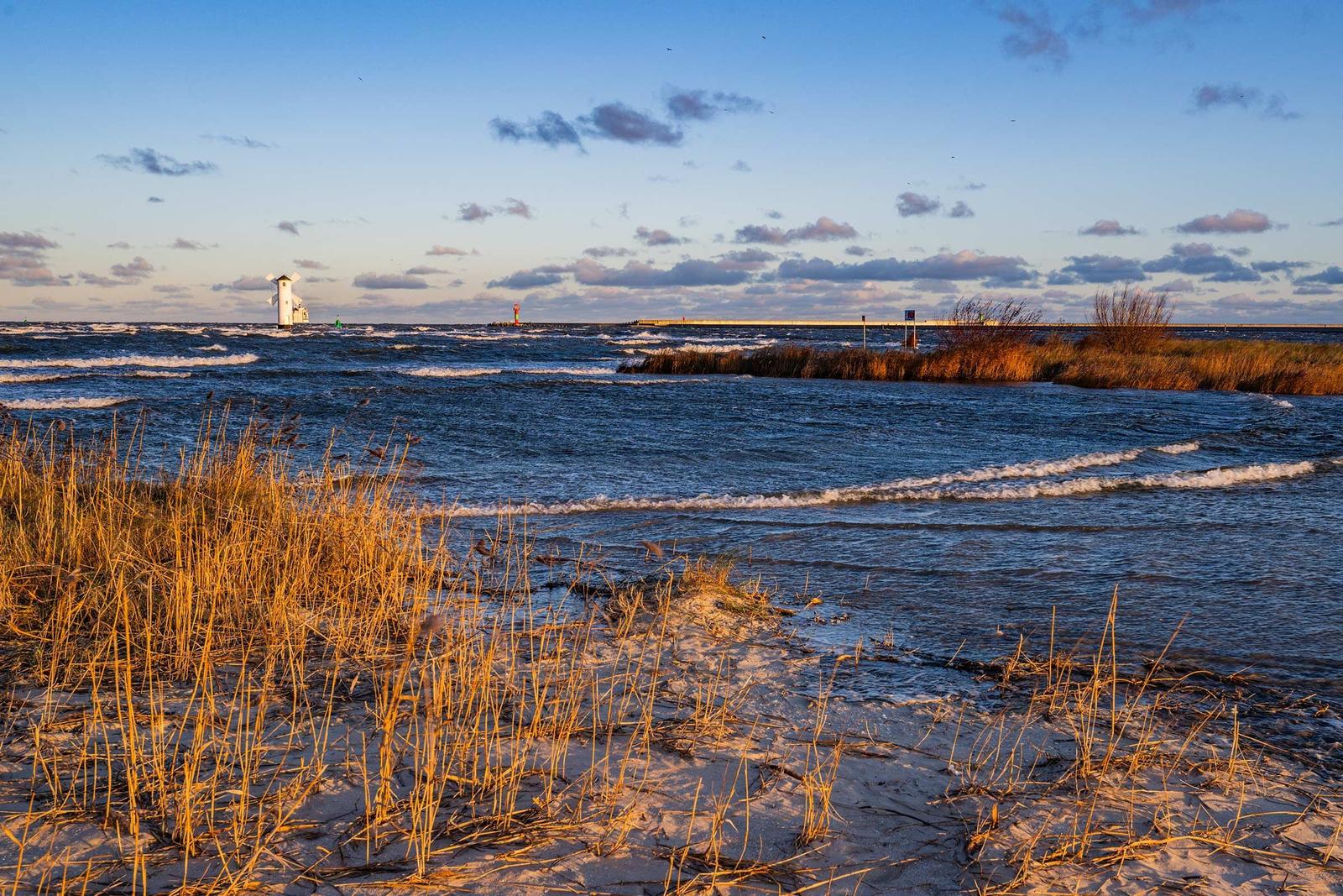 Holzbank am Strand mit Blick aufs Meer und Leuchttürme im Hintergrund.