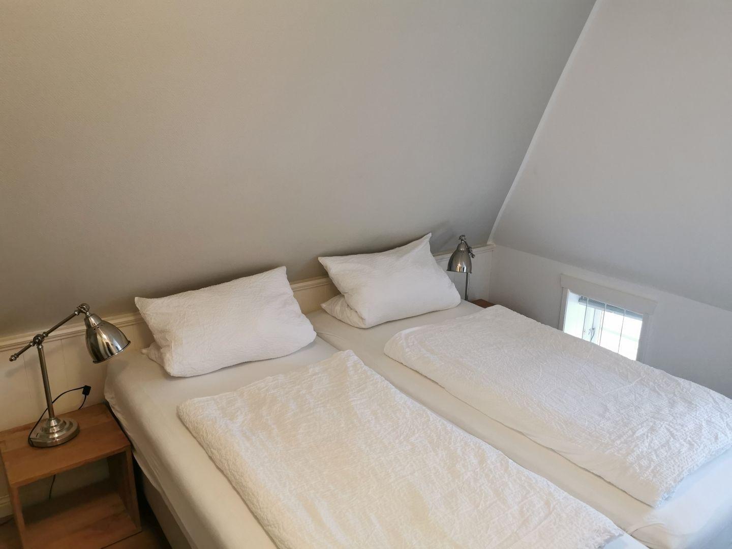 Schlafzimmer mit Doppelbett, weißen Bettwäsche, Schrank und Stuhl unter Dachschräge.