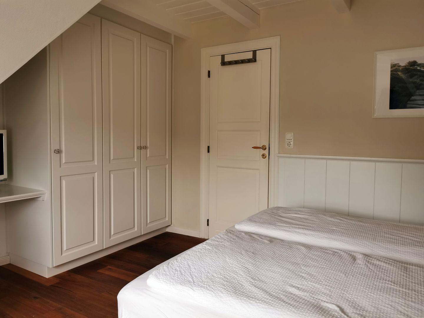 Schlafzimmer mit Dachschrägen, Bett, Schrank, Schreibtisch und Stuhl.