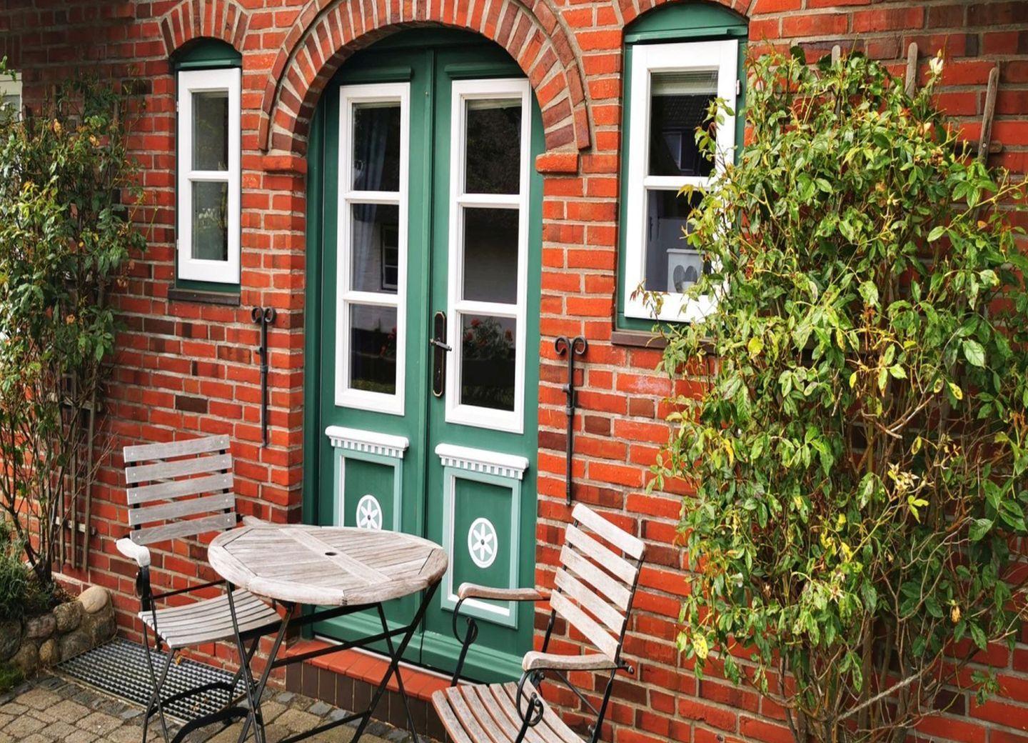 Rotes Backsteinhaus mit Strohdach, Garten mit Blumen und Terrasse.