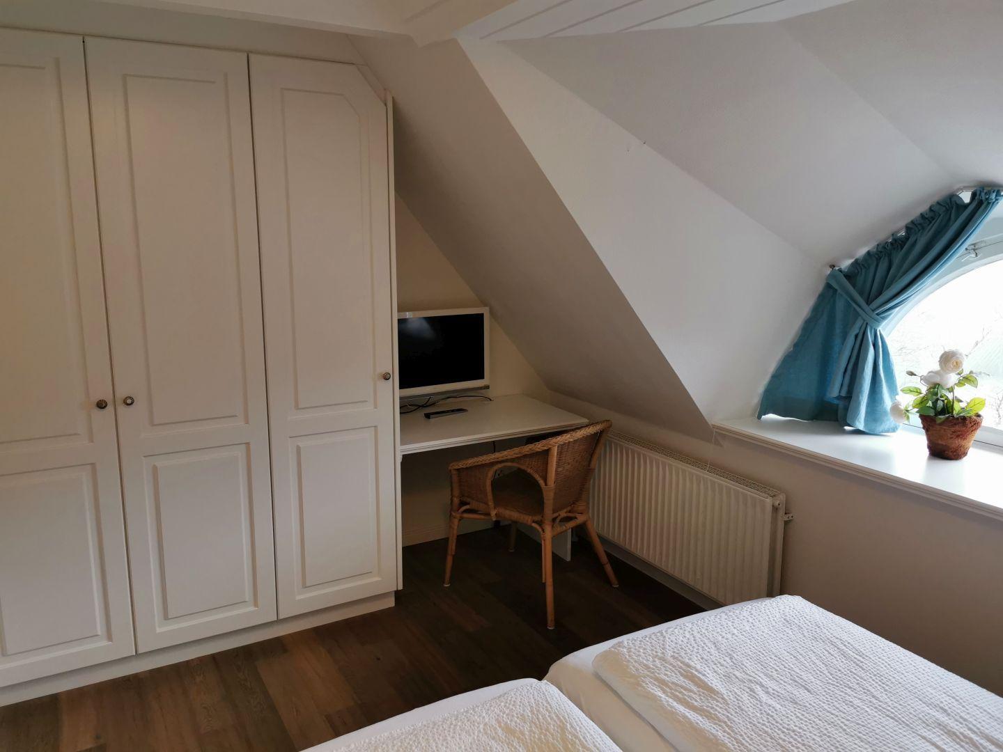 Doppelbett mit weißen Bettwäsche, zwei Nachttische mit Lampen und Fenster mit blauen Vorhängen.