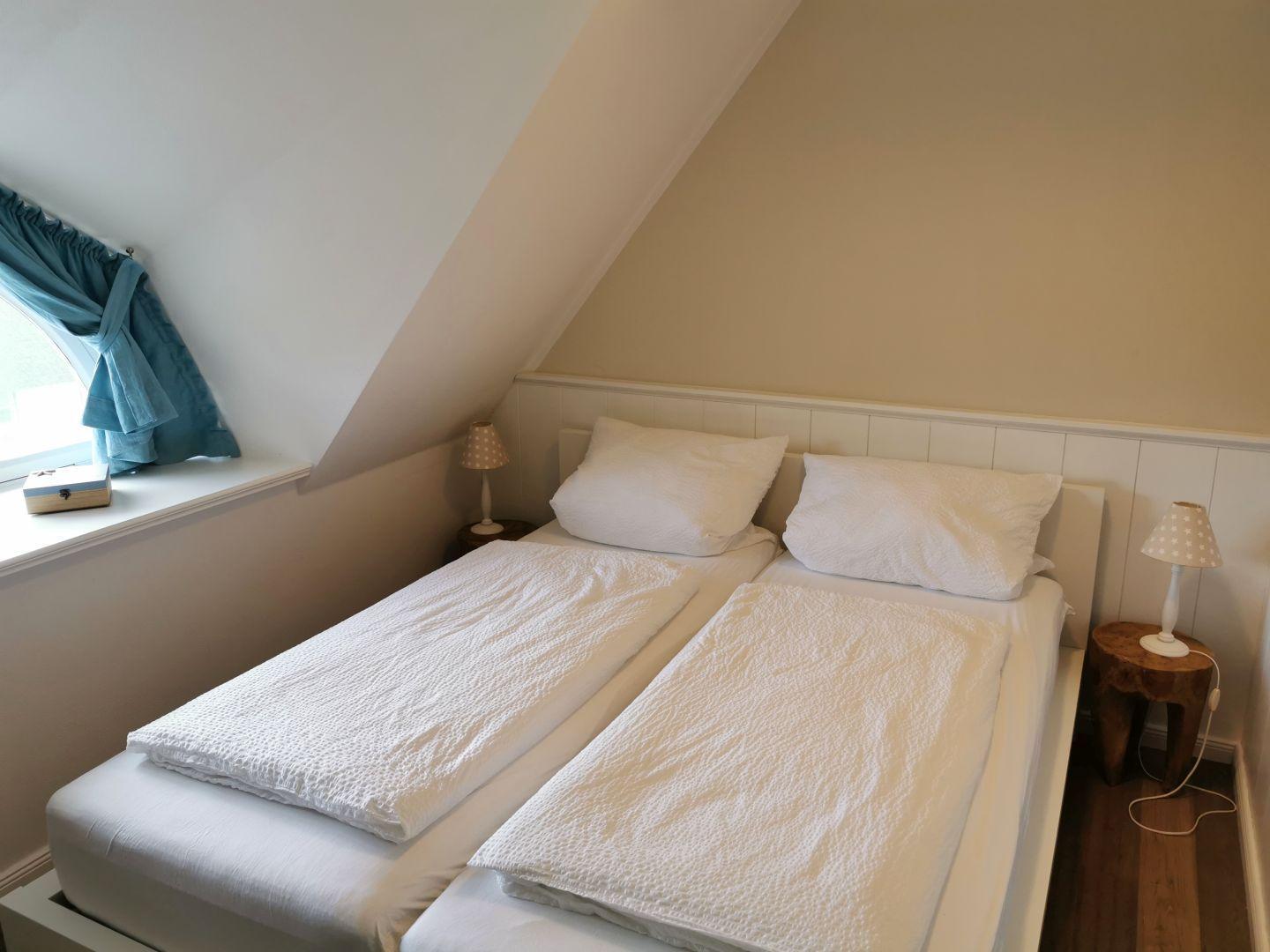 Zwei Betten mit weißen Bettwäschen, Wandbilder und Nachttisch mit Lampe.