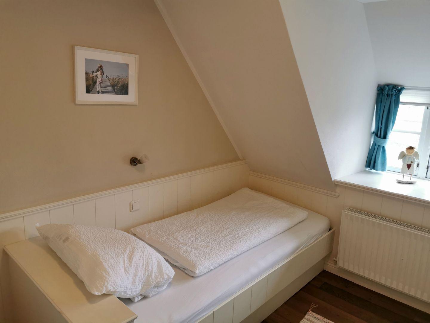 Ein Schlafzimmer mit Dachschrägen, Fenster mit blauen Vorhängen und einem Bett mit weißer Bettwäsche.