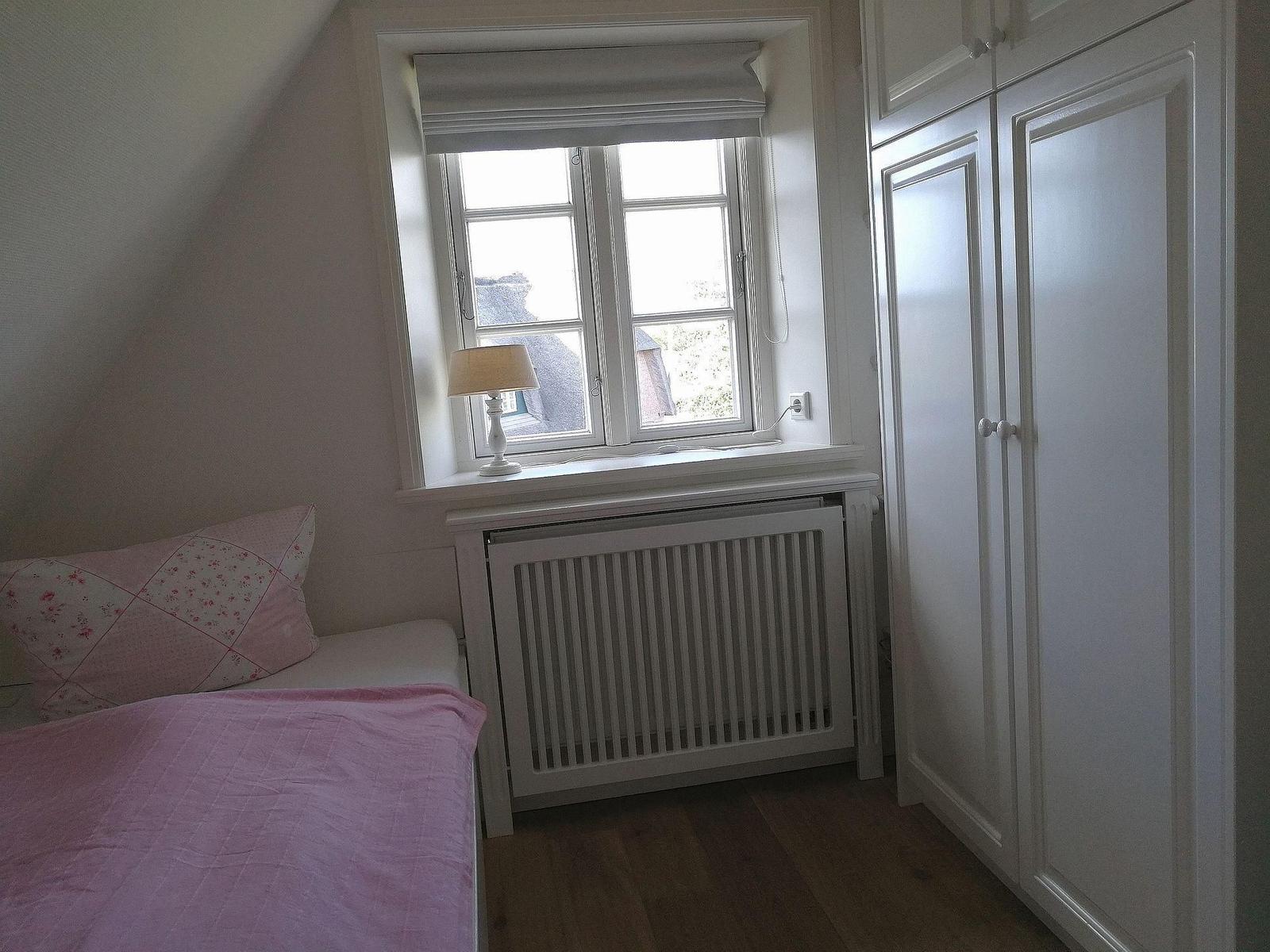Schlafzimmer mit Bett, rosa Bettwäsche und weißem Schrank.
