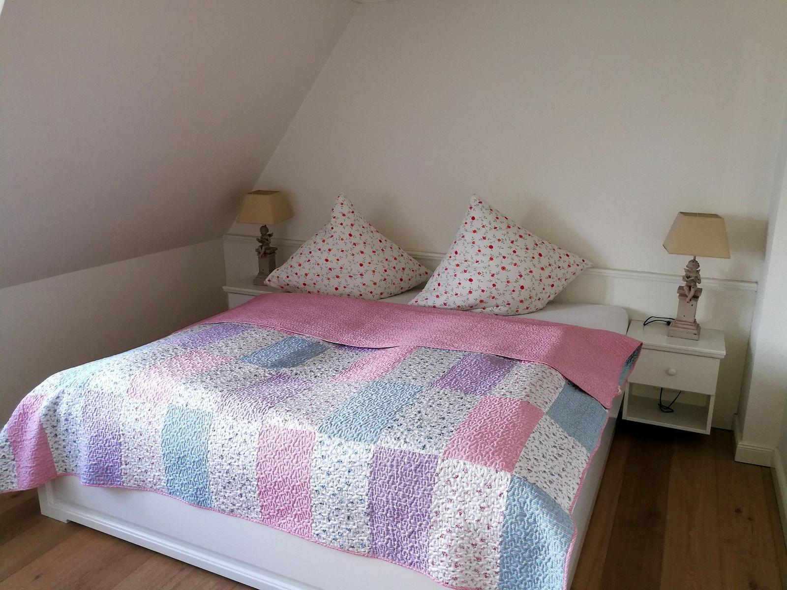 Schlafzimmer mit Kleiderschrank, Fenster und Bett mit buntem Decken.