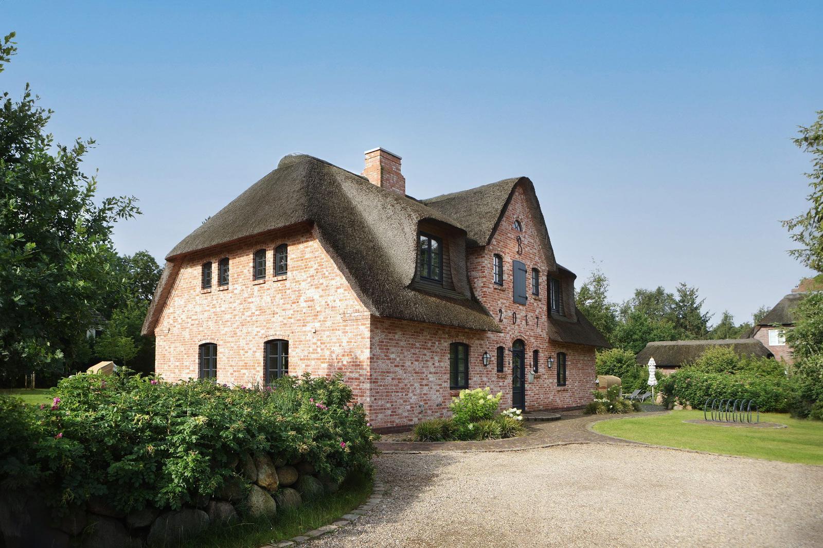 Haus mit Strohdach, Garten und Terrasse. Umgeben von Wald und Grünflächen.