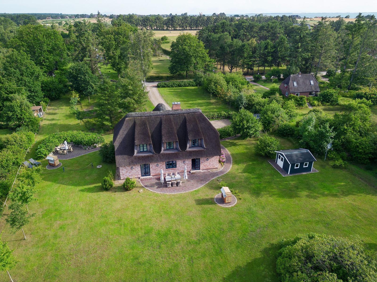Haus mit Strohdach und Garten. Umgeben von Wald und Grünflächen.