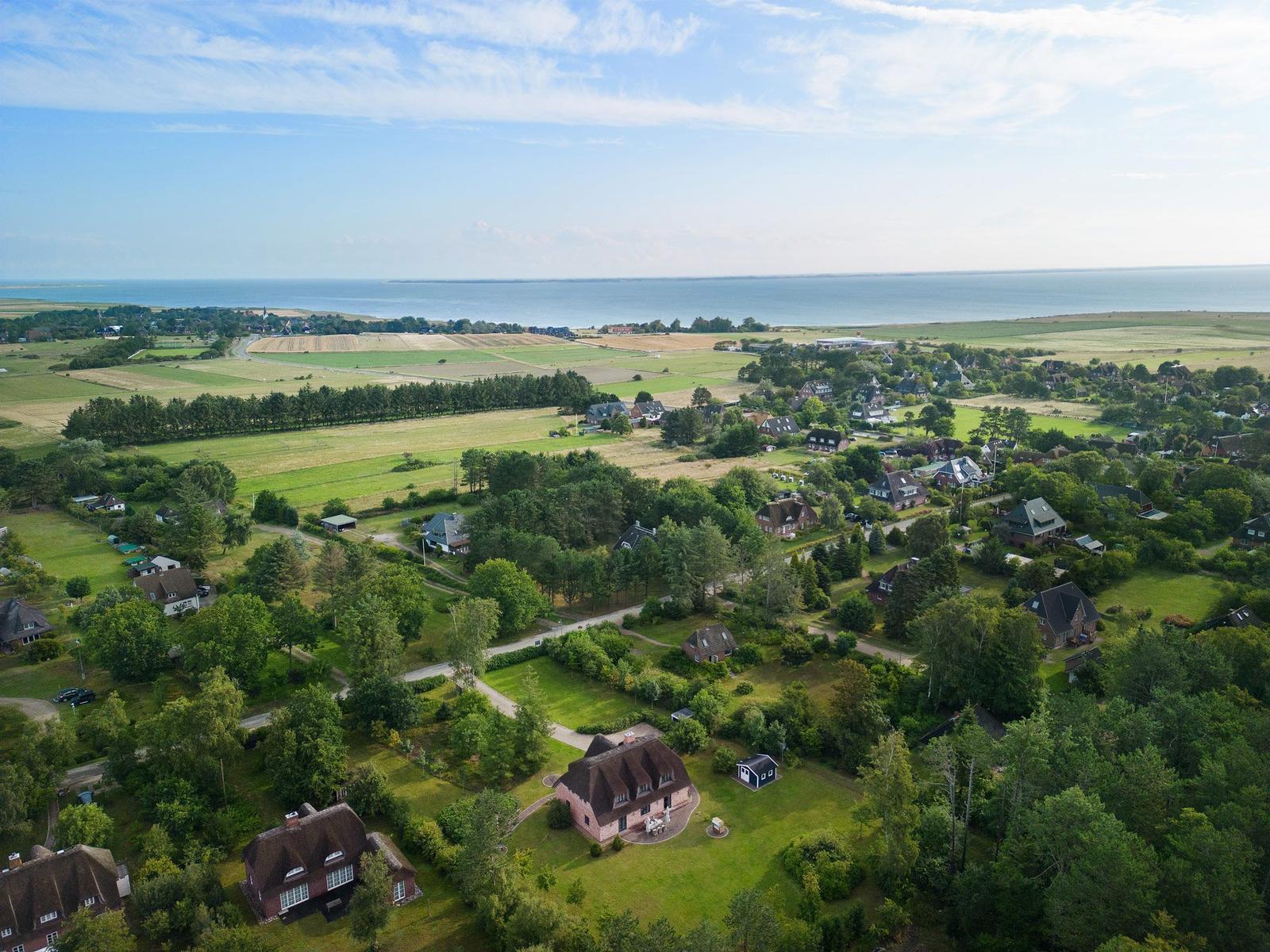Haus mit Garten, Wald und Leuchtturm im Hintergrund