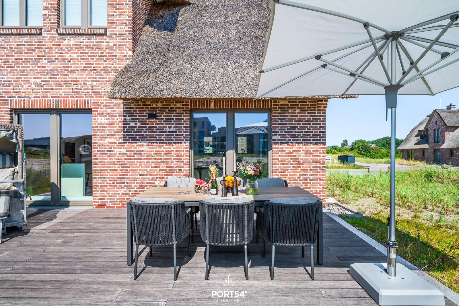 Haus mit strohgedecktem Dach und Holzgarage auf gepflasterter Fläche