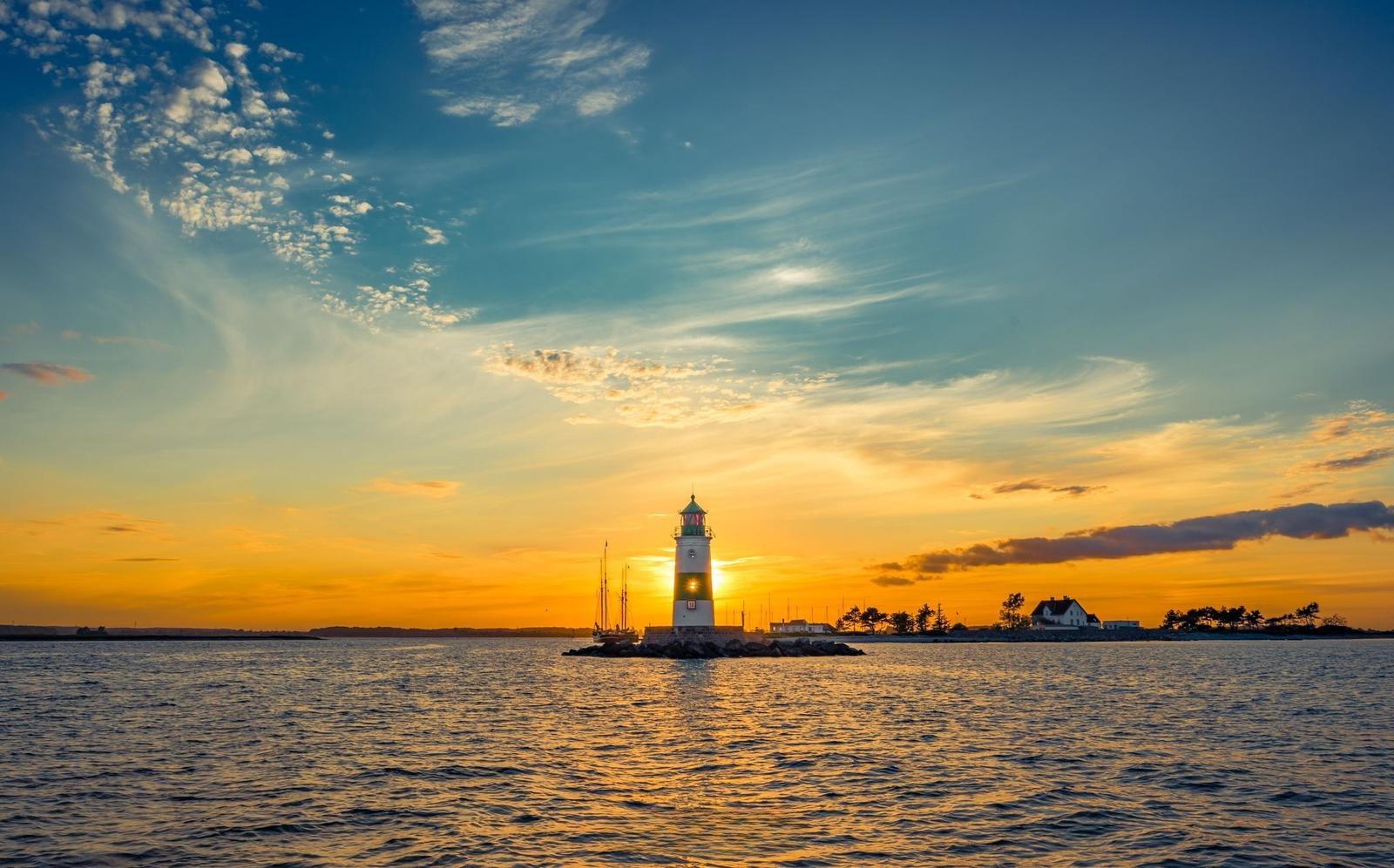 Sonnenuntergang über ruhigem Wasser mit Windkraftanlagen am Horizont.